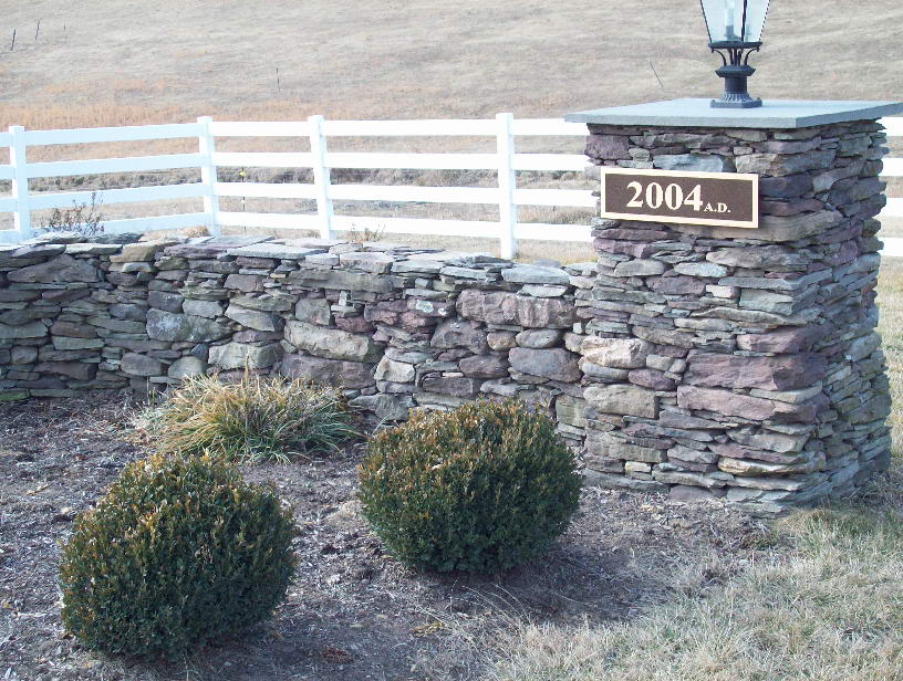 Dry stacked stone estate entrance wall and boxwood bed